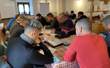 Diversi uomini seduti a un tavolo con tovaglia a quadri scrivono durante un team coaching
