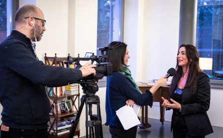 Uomo filma donna con videocamera mentre intervistatrice tiene microfono