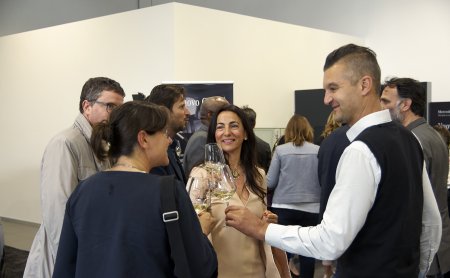 Gruppo di persone in una stanza con pareti bianche che brindano e conversano