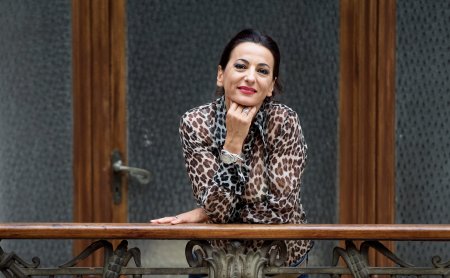 Donna sorride appoggiata a una ringhiera in metallo decorata davanti a una porta di legno