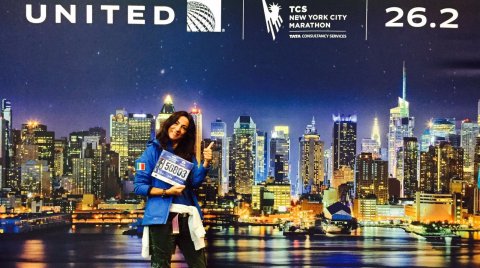 Frau mit Startnummer vor beleuchteter New Yorker Skyline bei Nacht, Marathon-Logos oben
