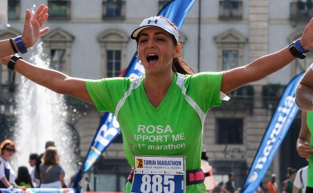 Donna con maglietta verde e numero 885 festeggia con le braccia aperte alla maratona di Torino